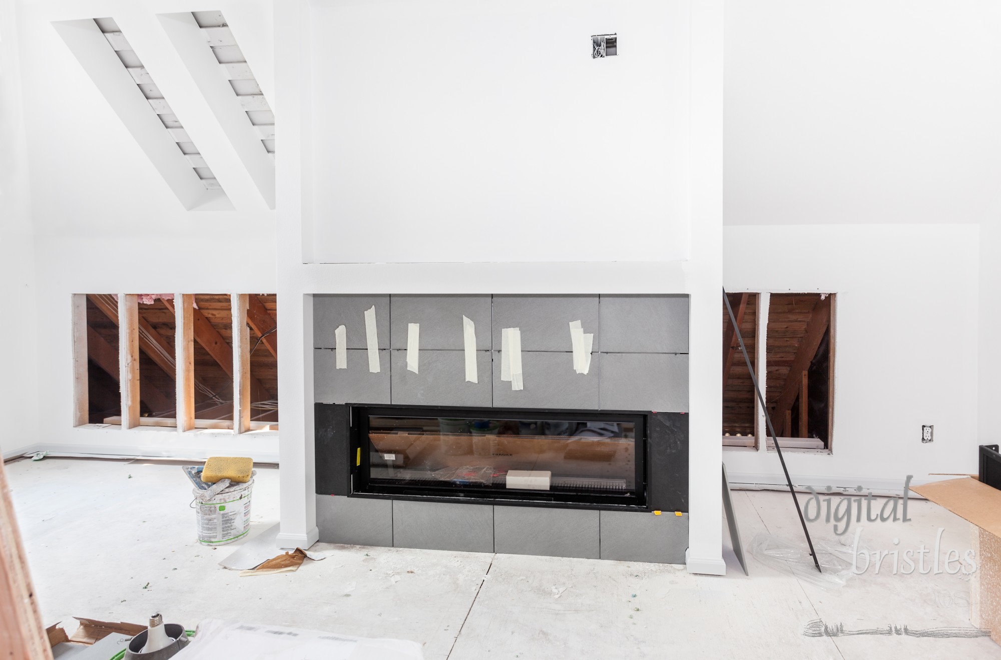 Gray and black tiles form the face of a new fireplace. Cutouts with supports for new bookcases, and finished openings for new skylights