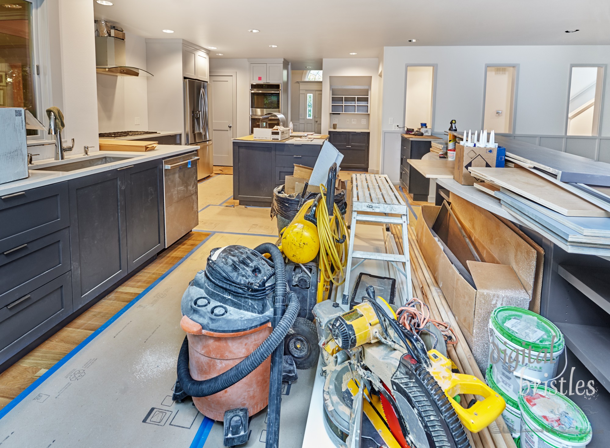 In-progress kitchen remodel with tools and supplies organized at the end of the day. Appliances and countertops in place; family room shelves awaiting installation